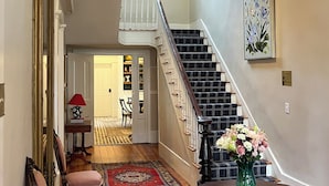 A grand staircase with a black and white striped carpet, a chandelier, and a framed floral painting on the wall. - Luxury Private Suite in Boutique Historic Inn The Athenian -Downtown Location (Athens)