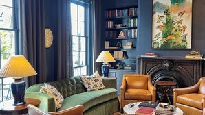 Un salon chaleureux avec un canapé vert, des fauteuils en cuir, une cheminée, une bibliothèque et un grand tableau.