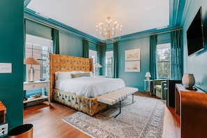 A bedroom with a bed, a bedside table, a lamp, a chair, a rug, and a television.
