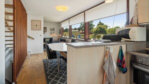 Eine moderne Küche mit integriertem Mikrowellenherd, einem Essbereich mit Tisch und Stühlen sowie Blick ins Freie durch große Fenster.