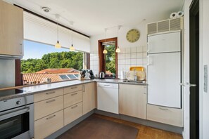 A modern kitchen with built-in appliances, a window with a view of greenery, and pendant lighting. - Cosy house near forest and coast (Svaneke)