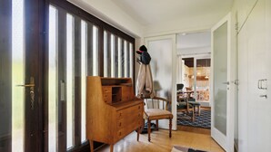 Ein Zimmer mit einem Holzkapuzen, einem Stuhl, einem Kleiderständer und einer Tür zu einem anderen Raum.