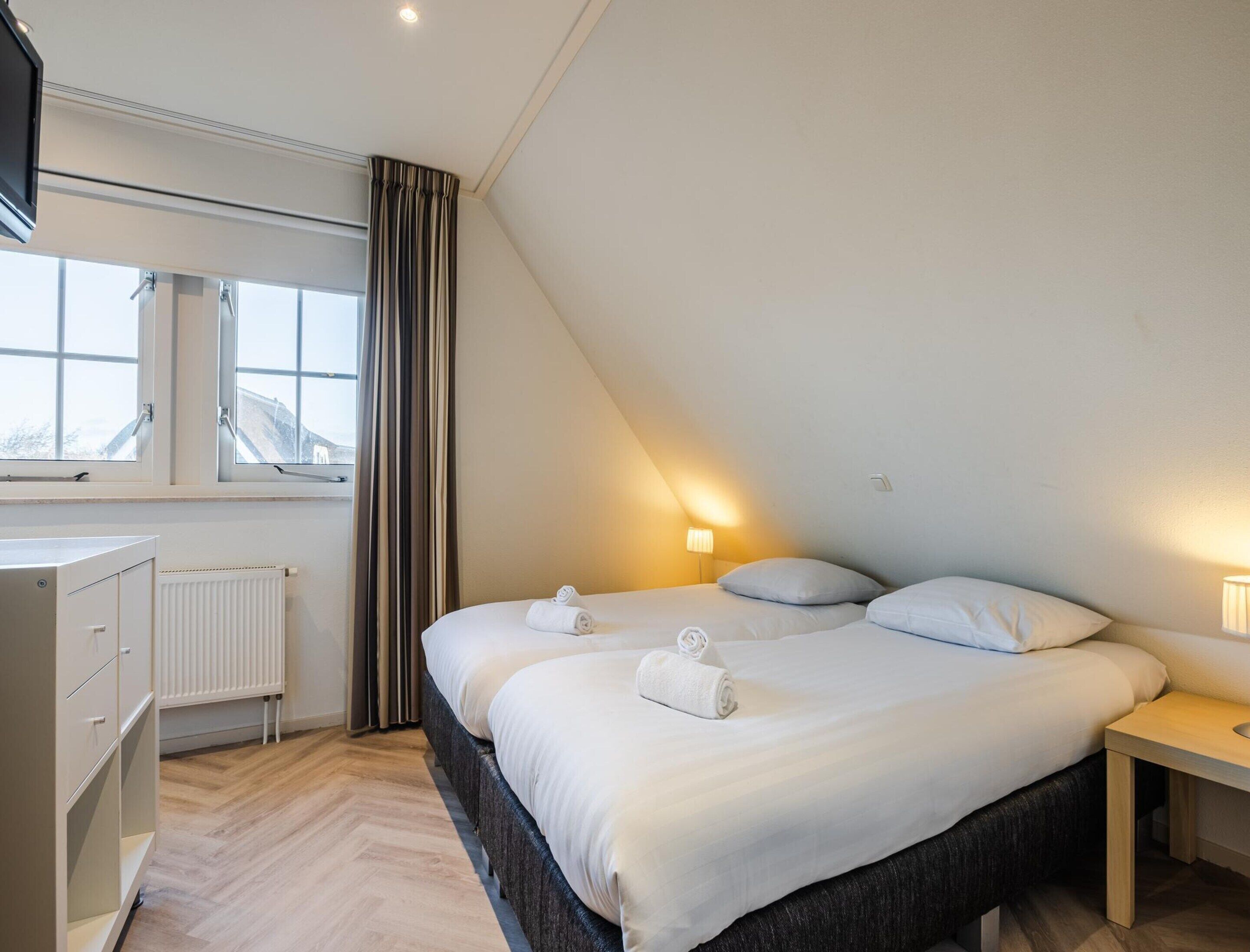 A modern bedroom with a large bed, a dresser, a radiator, and a window with curtains.