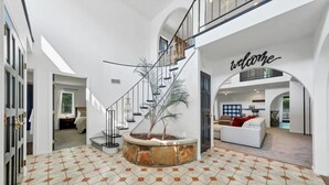 A spacious interior with a central staircase, a living area with a white sofa, and a 'welcome' sign on the wall.