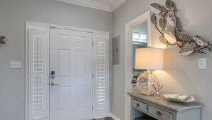Un couloir avec une porte blanche, un miroir et une lampe sur une commode.