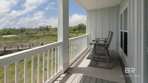 Une véranda couverte avec une balustrade blanche, un banc et une vue sur un paysage verdoyant.
