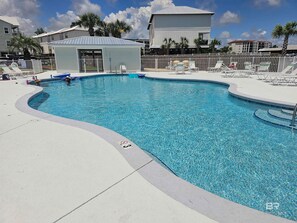 Una piscina con sillones de descanso y un pequeño edificio, rodeado de palmeras y casas.