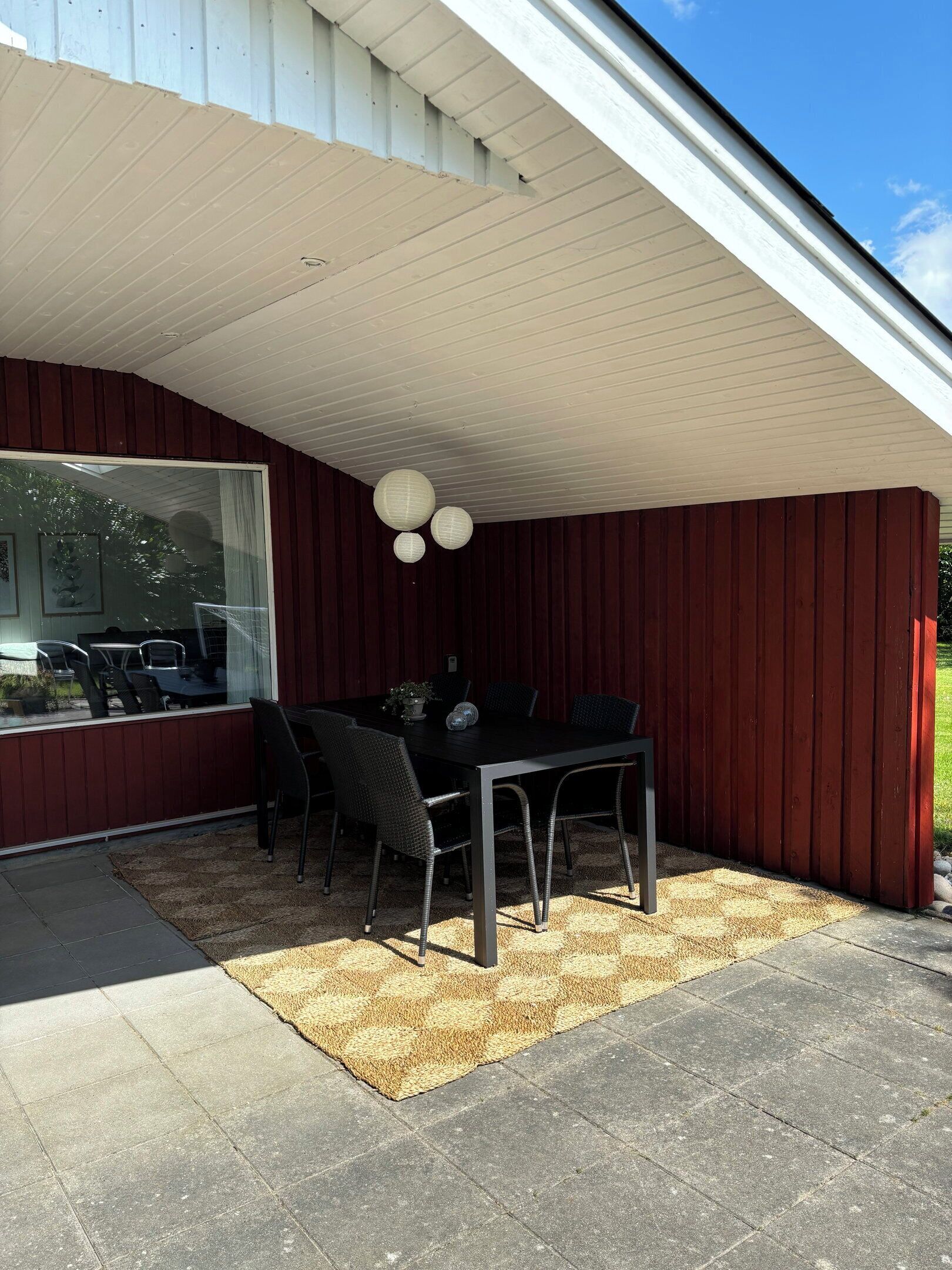 A covered patio with a dining table and chairs, a large window, and a ceiling with a light fixture.