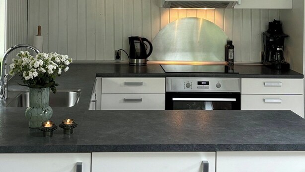 A modern kitchen with white cabinetry, a stainless steel sink, a Bosch range hood, and a black countertop. - Cozy cottage with a wilderness hot tub (Sydals)