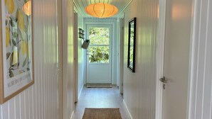 A hallway with white paneled walls, a wooden floor, a door at the end, and a hanging light fixture. - Cozy cottage with a wilderness hot tub (Sydals)