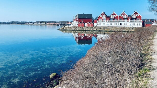 A waterfront building with multiple red and white structures, a calm lake, and a clear sky. - Luxury holiday home with sea view (Gråsten)