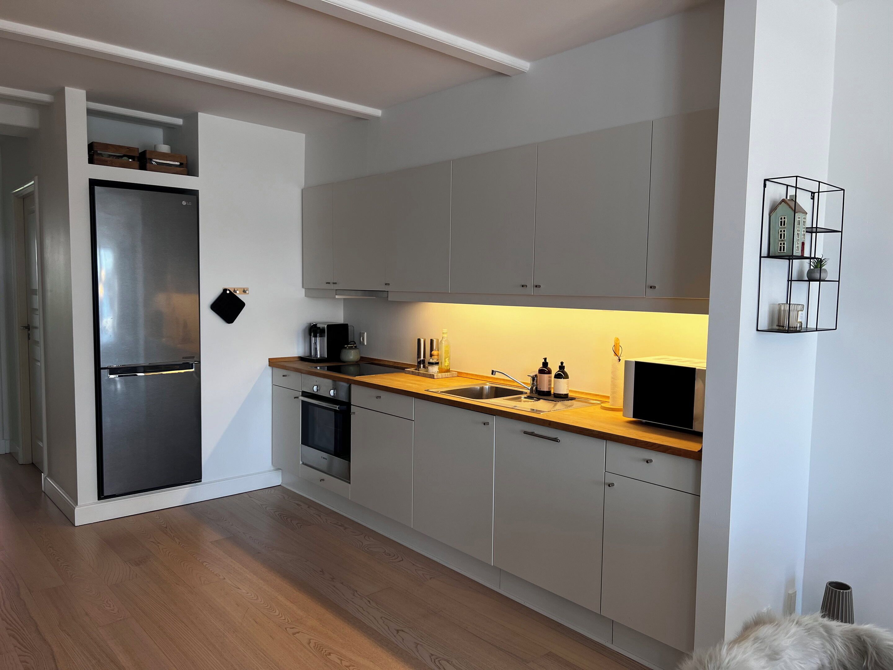 A modern kitchen with grey cabinets, a stainless steel refrigerator, a wooden countertop, and a built-in oven.