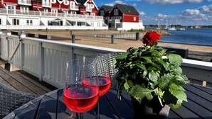 A coastal view with a row of red and white buildings, two glasses of red wine, and a potted plant on a deck. - Luxury holiday home with sea view (Gråsten)