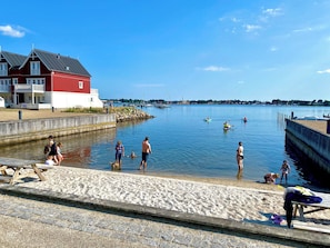 A waterfront area with a red building, sandy beach, and calm water.