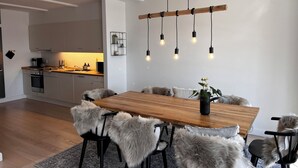 A modern dining area with a wooden table, black chairs, and a hanging light fixture. - Luxury holiday home with sea view (Gråsten)