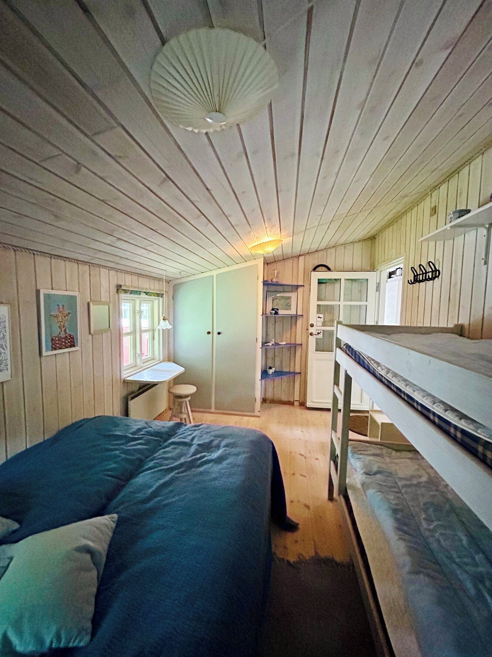 A room with a bunk bed, a desk, a chair, and a shelf with various items.