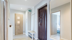 A hallway with a wooden door, a white bench, and a doormat with a house symbol. - Winogrady Stylish Apartment (Poznań)