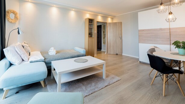 A modern living room with a sofa, coffee table, and dining area. - Winogrady Stylish Apartment (Poznań)