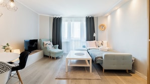 A modern living room with a sofa, armchair, and coffee table. There is a TV, a lamp, and a window with curtains. - Winogrady Stylish Apartment (Poznań)
