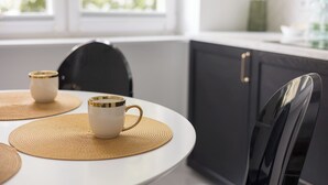 A modern kitchen with a round white table, two white cups with gold rims, and a black chair. - Chmielna Green Apartment (Warszawa)