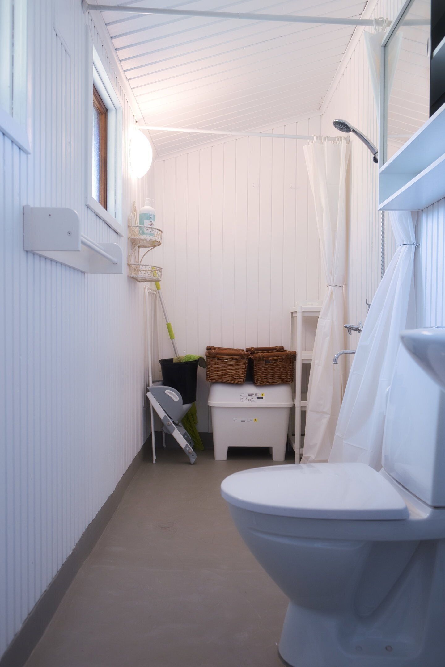 Un baño estrecho con inodoro blanco, cortina de ducha y un pequeño estante con cestas.