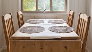Una mesa de comedor con cuatro individuales, sillas de madera, una lámpara colgante y una ventana con vistas a vegetación.