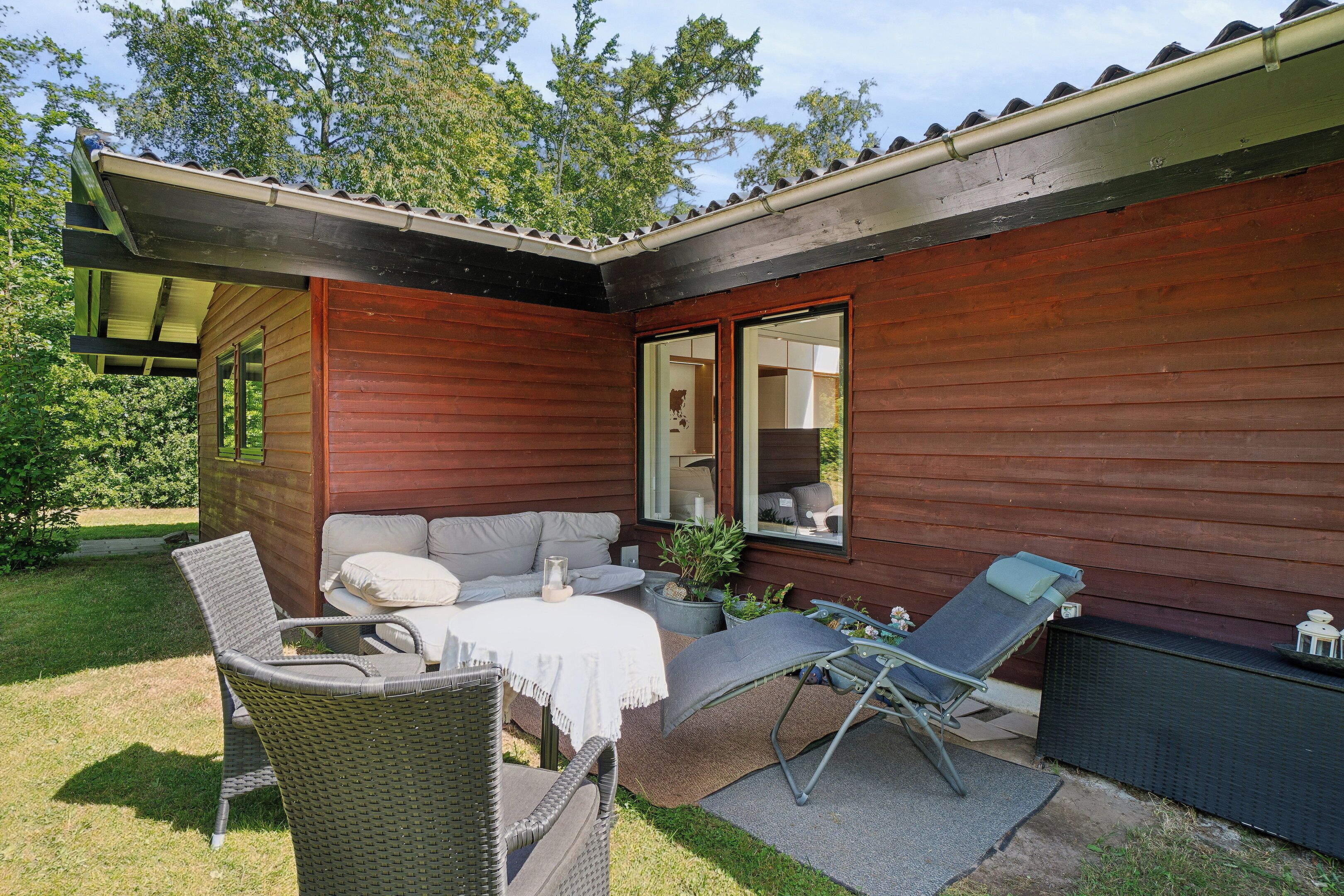 A wooden cabin with a patio area featuring wicker furniture, a table, and potted plants.