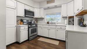 Una cocina con armarios blancos, una estufa de acero inoxidable, un microondas y una ventana con vistas a árboles.