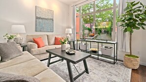 A modern living room with a sofa, coffee table, and a large window with a view of greenery. - The Cozy Corner Retreat 15 min Walk to Old Town (Fort Collins)