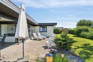 Une maison moderne dotée d’un patio, d’un espace salon extérieur et d’un jardin.