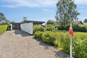 A modern house with a gravel driveway, a red flag, and lush greenery.