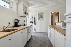 A kitchen with white cabinetry, a wooden countertop, a dishwasher, a coffee maker, and a microwave.