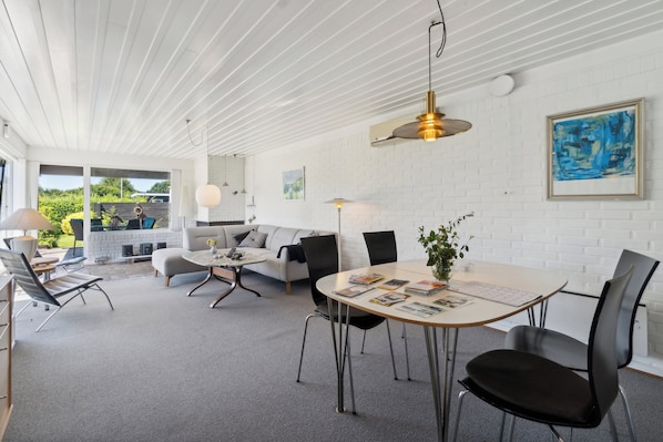 A modern interior with a dining area, a sofa, and a view of the outdoors.