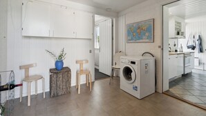 A laundry room with a washing machine, wooden chairs, a small table with a vase, and a map on the wall. - Atmospheric summer cottage at Hejlsminde (Hejls)