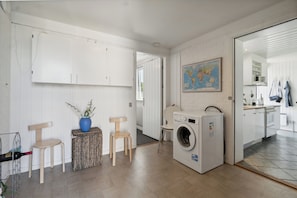 A laundry room with a washing machine, wooden chairs, a small table with a vase, and a map on the wall.