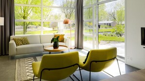 A modern living room with a sofa, two yellow chairs, a coffee table, and large windows offering a view of a green landscape. - Modern Holiday Home With a Deco Fireplace (Enkhuizen)