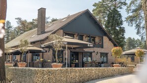 A two-story building with a brick facade, a tiled roof, and outdoor seating with umbrellas. - Nice Chalet With Dishwasher, Maastricht at 16 km (Zutendaal)