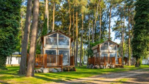 Two wooden cabins with balconies, surrounded by tall trees and a dirt path. - Nice Chalet With Dishwasher, Maastricht at 16 km (Zutendaal)