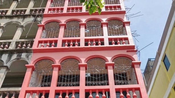 A multi-story building with a red facade, large arched windows with metal grilles, and a balcony with balustrades. - LZ Hostel (Bangkok)