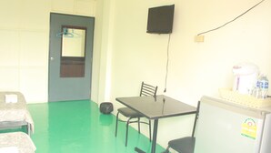 A small room with a table, chairs, a refrigerator, a hanging coat rack, and a wall-mounted speaker. - LZ Hostel (Bangkok)