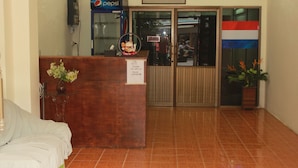 A reception area with a wooden desk, a Pepsi refrigerator, a glass door entrance, and a flag on the wall. - LZ Hostel (Bangkok)