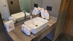 A modern bathroom with a large white sink, a mirror, and multiple towels with the Play Motel logo. - 4Play Motel (El Marques)