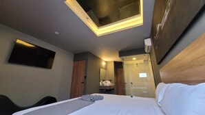 A hotel room with a bed, a desk, a TV, a mirror, a bathroom with a shower, and a ceiling light. - 4Play Motel (El Marques)