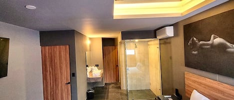 Habitación de hotel moderna con una cama grande, baño con ducha de vidrio y vistas a la ciudad.