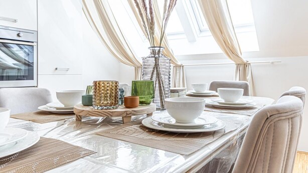 Et spisebord dækket med hvide tallerkner og skåle, en vase med tørrede planter og en høj glassvase.
