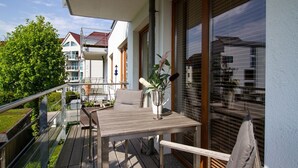 Un balcón con mesa y sillas de madera, una planta en maceta y vistas de edificios vecinos.