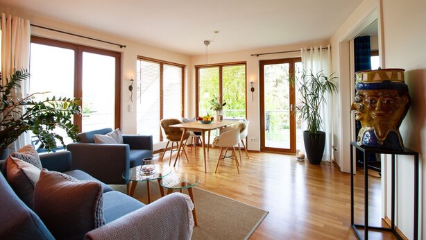 Un amplio salón con un conjunto de sofás, una mesa de comedor y un gran ventanal con persianas.