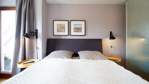 Un dormitorio moderno con una cama grande, dos mesitas de noche, una ventana con cortinas y dos cuadros enmarcados en la pared.
