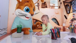 A person sitting at a table with a large rabbit mascot, surrounded by drawing materials and a notebook. - Holiday Home in Bad Bentheim Near Dutch Border (Bad Bentheim)