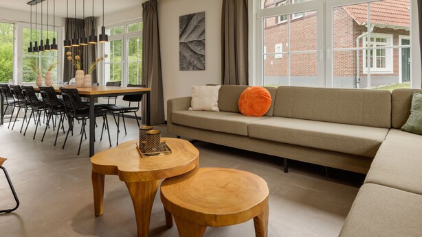 A modern living room with a sofa, a dining table with chairs, and a large window with a view of a brick building. - Holiday Home in Bad Bentheim Near Dutch Border (Bad Bentheim)